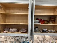 Cabinet shelves with stacks of vintage Johnson Brothers plates and bowls, wood bowls, mugs, and glasses inside.