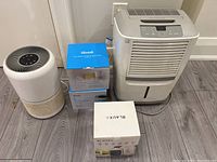 Frigidaire dehumidifier, Levoit air purifier, two Levoit filter boxes, and Blaux fan box arranged on floor.