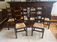 Six wooden dining chairs with ladder backs and wicker seats arranged in a row, showing front view and overall lot.