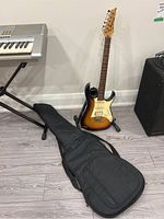 Full view of guitar on stand with soft case on floor and keyboard in background