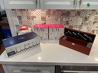 Lot contents on countertop including boxed Mikasa stemless wine glasses, boxed LAV champagne flutes, wooden box with barware, and some napkins stacked.