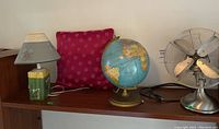 Full view of the four items: globe, lamp, pillow, and fan on a wooden shelf