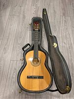 Full view of Steves acoustic guitar inside open lined hard case on wooden floor.