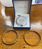Set of two Mexican silver bracelets with hammer texture, one with visible stamped markings, and a Rachel Zoe adjustable silver necklace placed inside its branded box.