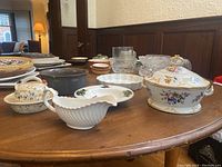 View of assorted dishes on wooden table showing porcelain tureen, Denby bowl, gravy boat, glassware and plates.