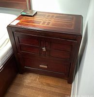 Full side view of dark wood side table with two drawers, square and rectangular metal handles, and patterned inlay top.