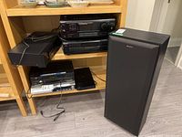 Overall photo of Sony AM FM receiver, CD player, cassette player stacked on wooden shelf with Sony speaker on floor.