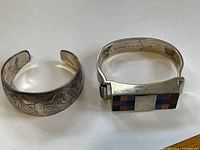 Two sterling silver bracelets, one cuff with engraved designs and one hinged with inlaid faux stones.
