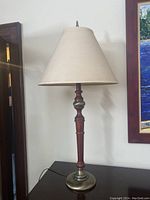 Full side view of the table lamp showing the turned wood and metal base, beige fabric shade, and finial on top.