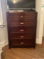 Front view of tallboy dresser showing five drawers with metal handles and dark wood finish.