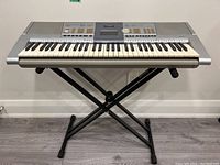 Front view of Yamaha PSR-293 electric piano on Apex adjustable stand showing 61 keys, speakers, buttons and LCD screen.