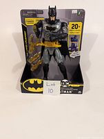 Front photo of Batman action figure in packaging showing yellow weapons and packaging text indicating 20+ phrases and sounds.