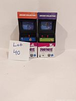 Two Fortnite Victory Royale Series figures in original unopened arcade collection packaging, showing front arcade cabinet design with joystick and character dancing on screen.