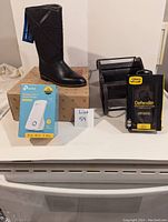Wide shot showing all items: women's black boot, TP-Link WiFi range extender box, black wooden organizer, and OtterBox Defender phone case.