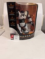 Robosapien robot toy in black and white in original sealed box, front view showing robot and remote.