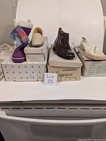 Front view of multiple shoe boxes stacked with visible shoes on top including white slip-ons, brown boots, purple canvas shoes, and white woven shoes.