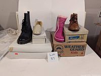 Lot showing 4 pairs of shoes and boots on top of their original boxes with some wear from storage