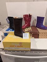 Four pairs of vintage new old stock boots displayed on boxes showing wear and damage. Includes black, brown, red, and purple boots.