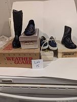 Lot of 8 pairs of vintage shoes and boots, black leather tall boots on a Weather Guard box, colorful beaded slip-ons on a Parkrids box, navy blue lace-up sneakers on a white box, black leather ankle boots on a separate box, displayed on a white surface with a lot number card