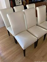 Six white leather dining chairs arranged on hardwood floor