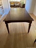 Solid wood rectangular dining table in good condition, showing wear and tear on the surface, photographed in natural light on a wood floor