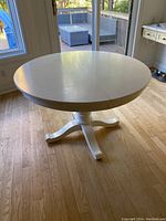 Full view of white round kitchen table with central pedestal base and expandable leaf split in the middle.