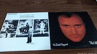Two vinyl album covers placed side by side on a wooden surface, showing Genesis and Phil Collins albums.