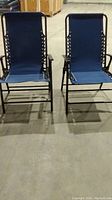 Two blue folding patio chairs standing side by side on a concrete floor, showing the full chairs from the front.