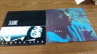 Two Sade vinyl albums: Diamond Life and Promise albums side-by-side on a wood surface.