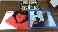Photo showing three vinyl rock albums including The Doors Greatest Hits, Blondie Eat to the Beat, and Glass Tiger album covers, laid out on table.