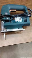 Side view of Black & Decker jigsaw showing blade, base plate, and power cord wrapped around handle.