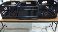 Front view of 3 black crates on a table, 1 Ikea and 2 typical milk crates, showing wear.