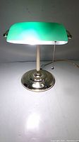 Front view of the green glass shade desk lamp illuminated, showing light and shade detailing.