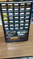 Front view of black plastic organizer caddy with multiple small drawers containing screws, bolts, nuts, and anchors.