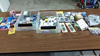 Overview of the lot items arrayed on a wooden table including plastic bins with various screws, fittings, clamps, and electrical components.