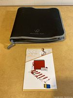 Closed black fabric carrying case with Wolfgang Puck logo on front and instruction manual placed beneath showing red handled tool illustration.