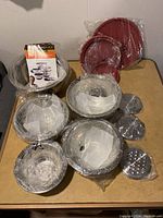 Photo showing all components wrapped in plastic including mixing bowls, lids, grater and slicing inserts, colander, and red plastic lids.