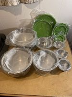 Overview of the stainless steel bowls overlapping and covered in plastic wrap, some green lids visible in background.