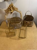 Four assorted gold-tone decorative baskets including one large oval wrapped in plastic with cherub decoration, smaller rectangular basket with cherub, a rectangular wire basket, and a small double compartment basket.