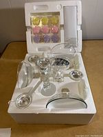 Glass candelabra centrepiece in original styrofoam packaging with components arranged and set of candles on top left corner.