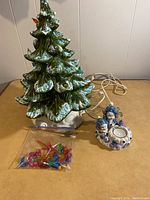 Green ceramic Christmas tree with white base and electrical cord, bag of plastic colored inserts, and winter scene candle holder with snowmen.