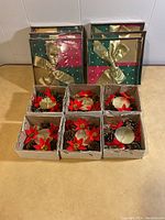 Six festive Christmas gift box kits wrapped in red, green, and gold paper with gold bows piled behind six square boxes each containing a Christmas candle holder decoration.