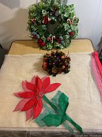 Photo showing two Christmas wreaths, mesh table cover with fabric poinsettia, and a Christmas centerpiece with brown fruits and berries