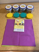 Four containers of Earth Brite Original Natural All Purpose Cleaner lined up with two yellow and two green circular sponge pads in front, and four microfiber cloths beneath them.