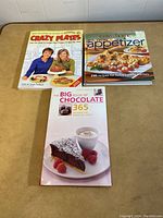 Three assorted cook books on a table, including Crazy Plates, The Ultimate Appetizer, and The Big Book of Chocolate.