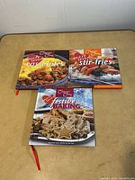 Three hardcover cookbooks set on a beige surface: Most Loved Casseroles, Stir Fries, and Festive Baking by Jean Paré. Covers show food pictures related to the titles.