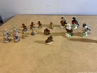 Overall photo showing entire collection of 15 small figurines arranged on a table including birds, gingerbread men, cats, and a ceramic house.