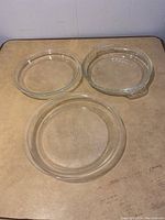Three glass pie plates arranged on a flat surface, showing various rim styles and clear glass material.