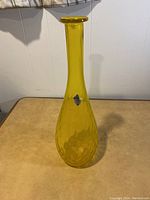 Front view of yellow glass vase on a table showing its teardrop shape and narrow neck with flat rim.