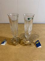 Front view of two clear crystal vases showing hand cut pattern and gold plated bases with original tags.